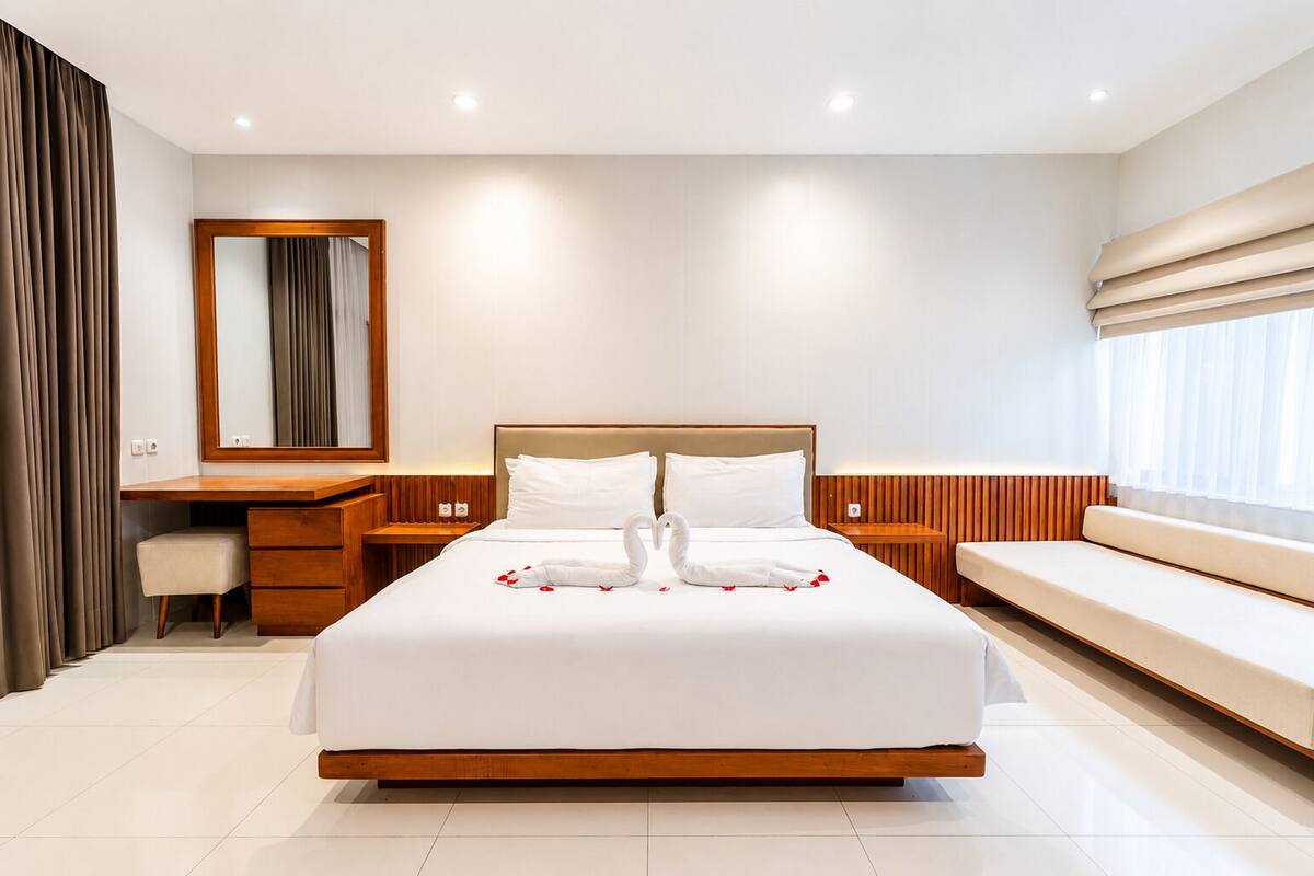 Una habitación de hotel moderna con una cama grande, un escritorio de madera, un banco y un espejo.