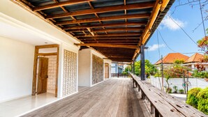 A covered outdoor corridor with wooden flooring, a bench, and a view of neighboring houses. - D' Green Nirava By Reccoma (Kabupaten Badung)