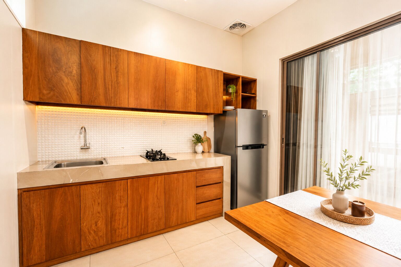 A modern kitchen with wooden cabinets, a stainless steel refrigerator, and a dining area with a table and plant.