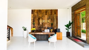 A reception desk with a wooden backdrop, two white wicker chairs, and a potted plant. - D' Green Nirava By Reccoma (Kabupaten Badung)