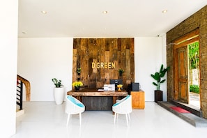 A reception desk with a wooden backdrop, two white wicker chairs, and a potted plant.