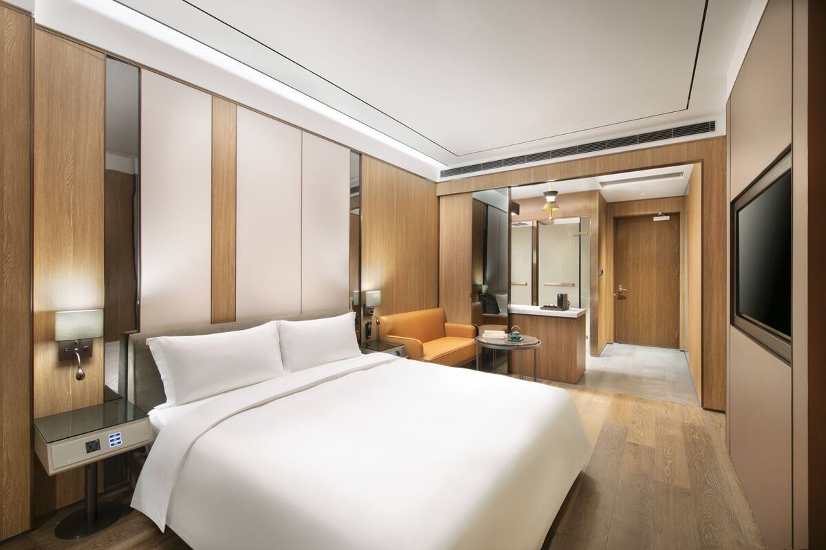 Habitación de hotel con cama, sofá, una mesita, televisor y baño visible a través de una puerta.