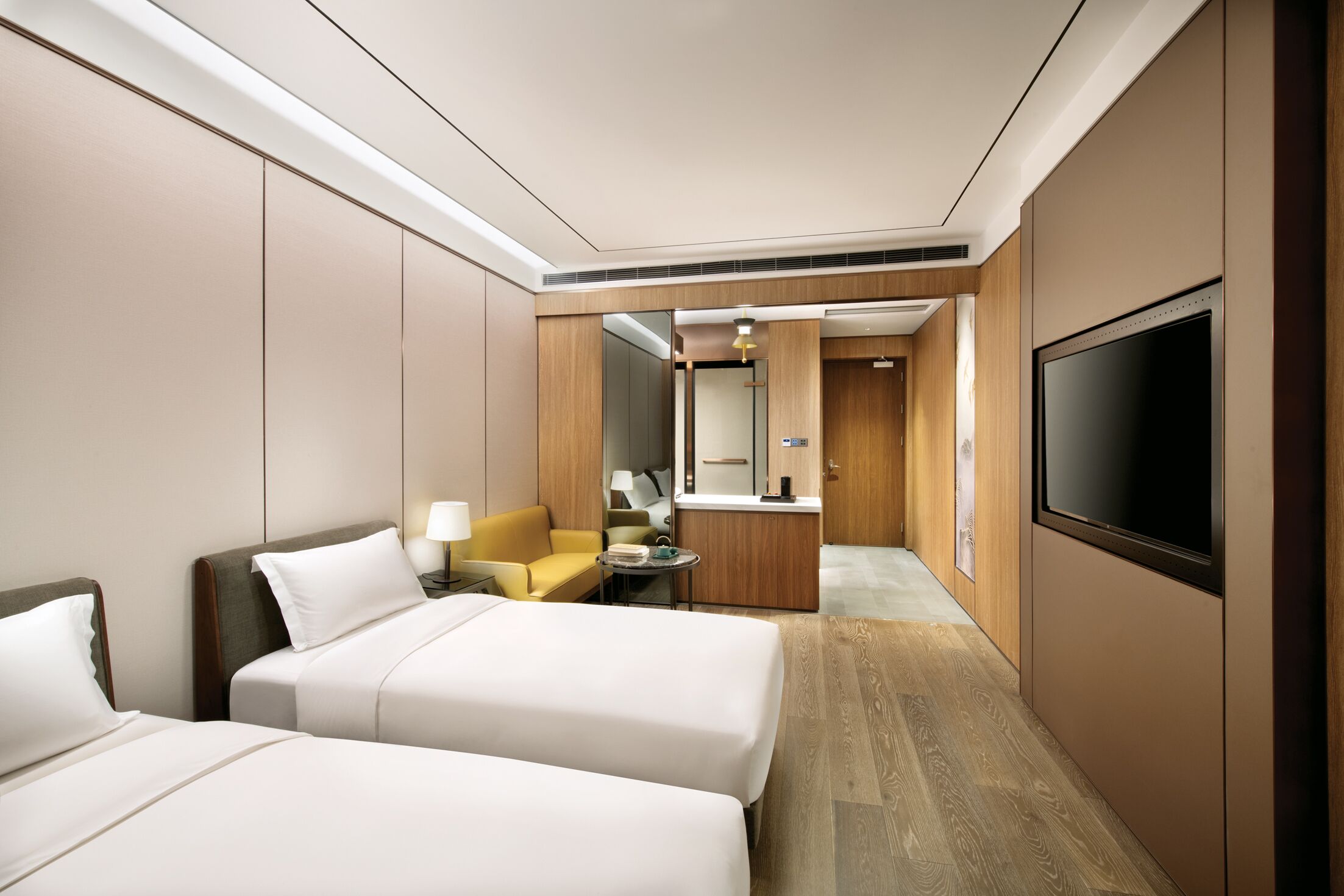 A hotel room with two beds, a sofa, a TV, a small table, and a kitchenette.