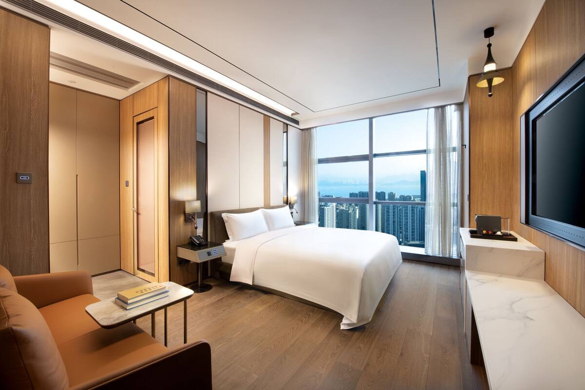 Una habitación de hotel moderna con una cama grande, un escritorio, un sofá y vistas a la ciudad.