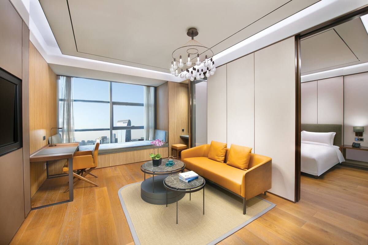Una habitación de hotel moderna con sofá, escritorio, silla, una mesita redonda y cama.
