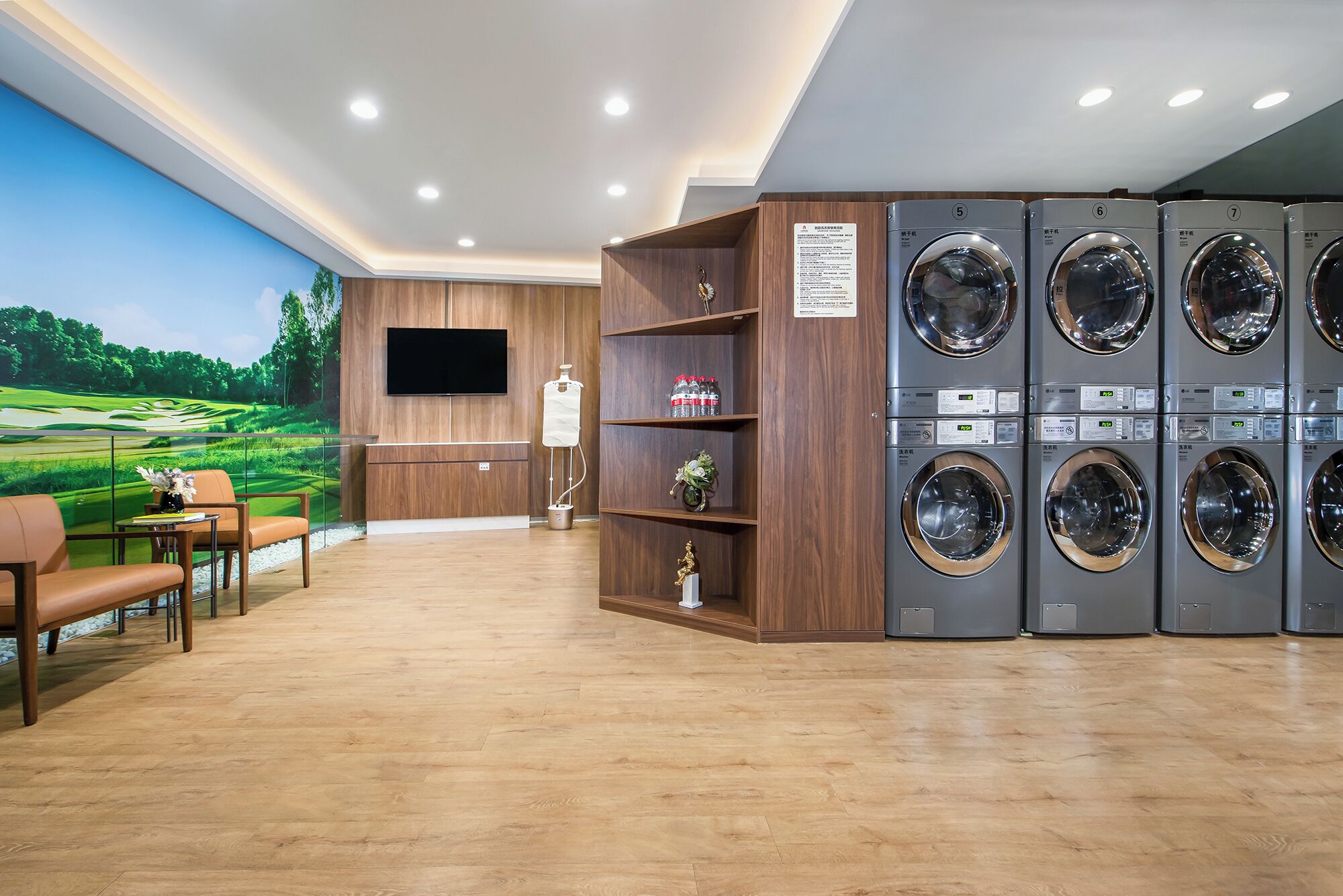 A laundry room with multiple washing machines, a wooden cabinet, a television, and a mural of a golf course.