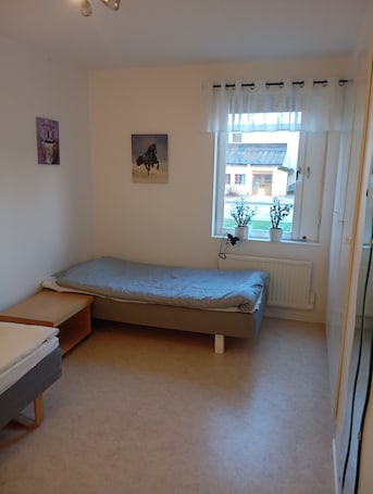 A bedroom with a single bed, a window with curtains, a radiator, and a small table.. Charming 2-bedroom Apartment in Historic Skara, Sweden