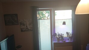Una habitación con piso de madera, un escritorio con computadora, una silla, una ventana con persianas y un radiador.