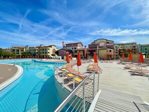 A swimming pool with lounge chairs and umbrellas, surrounded by colorful buildings. - Vibrant stay with shared outdoor pool (Città Metropolitana di Venezia)