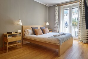 A modern bedroom with a wooden bed, bedside tables, a nightstand, and a view of the outside. - Fontana | The Rentals Collection (San Sebastián)