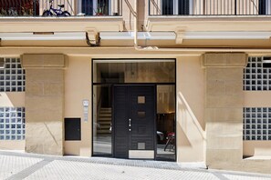A building facade with a black door, a visible staircase, and a numbered window. - Fontana | The Rentals Collection (San Sebastián)
