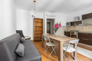 Een ruimtelijk ingerichte leefruimte met een bank, eettafel, stoelen, een keuken met fornuis en een boekenkast.