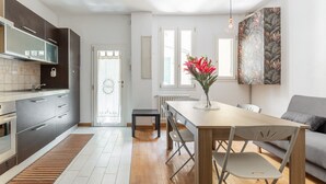 A modern kitchen with a built-in oven, a dining area with a wooden table and chairs, and a large window providing natural light. - Casa Centotrecento by Wonderful Italy (Bologna)