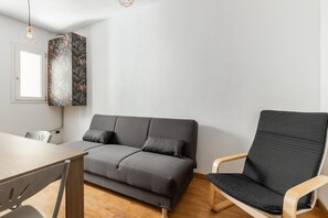 Een moderne kamer met een grijze bank, een houten stoel, een eettafel en een geometrisch lamp.