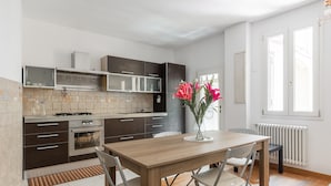A modern kitchen with dark cabinets, a wooden dining table, and a vase with flowers. - Casa Centotrecento by Wonderful Italy (Bologna)