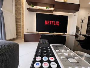 Un salon moderne avec un téléviseur affichant le logo « NETFLIX », une télécommande dotée de nombreux boutons et une étagère décorative placée au-dessus du téléviseur.