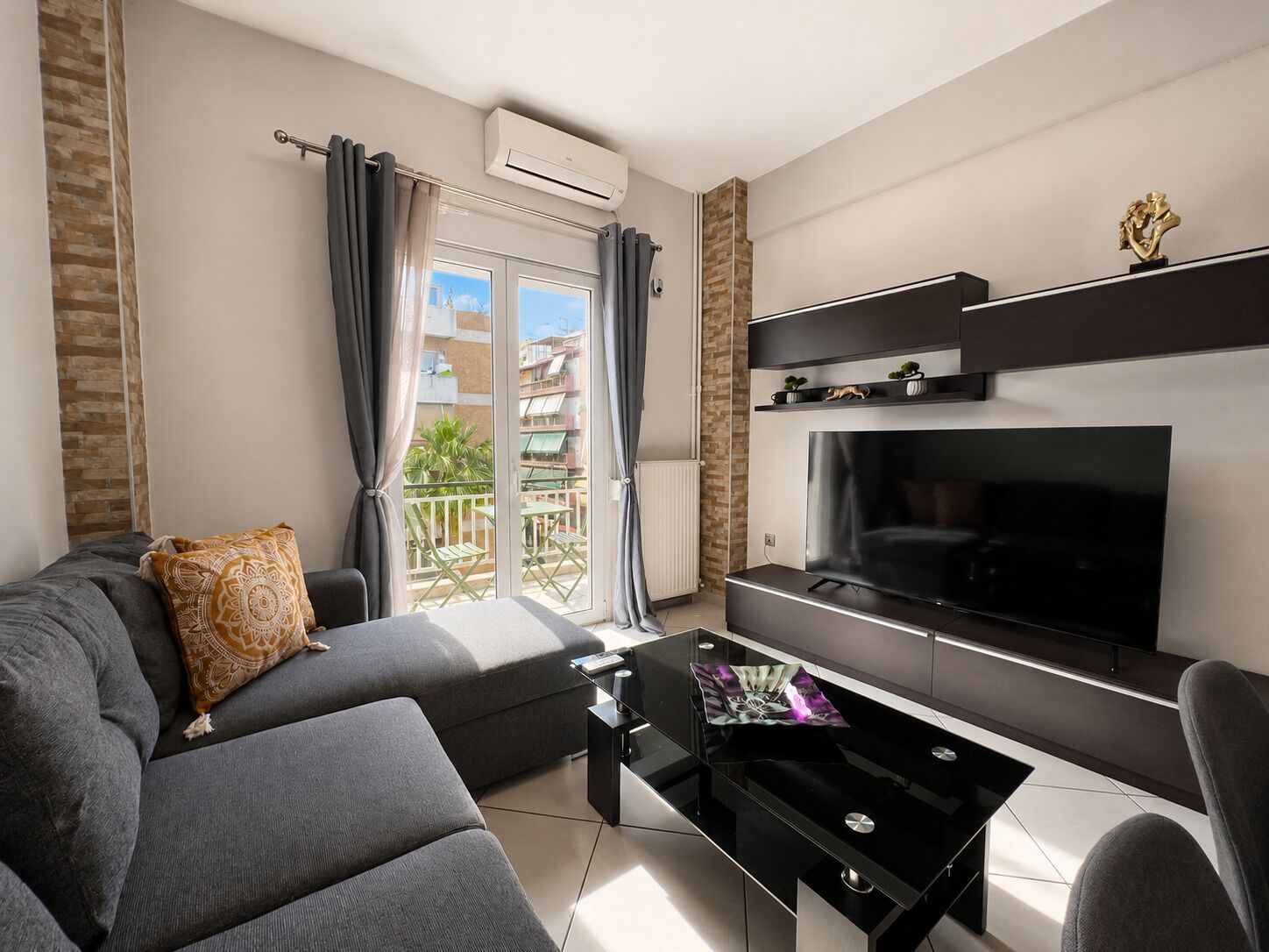 Ein modernes Wohnzimmer mit einer Couch, einem Couchtisch, einem Flachbildfernseher und einem Balkon mit Gartenmöbeln.