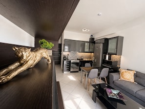 Une cuisine moderne avec des meubles de couleur sombre, un coin repas avec une table et des chaises, et un salon avec un canapé et une table basse.