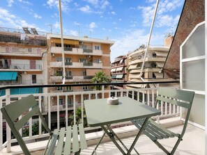 En balkon med bord og stole, der udover et boligområde med højhuse.