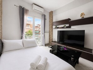 Une chambre d’hôtel comprenant un lit, un téléviseur à écran plat, une petite table, un balcon avec vue sur les bâtiments et un appareil de climatisation.