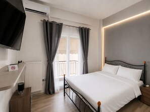 Et hotelværelse med en seng, et fjernsyn, en radiator, et vindue med gardiner og en balkon.