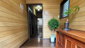 A wooden interior hallway with a reception desk, a potted plant, and a row of shoes on the floor. - Spacious 5BR Asakusa Riverside House near Sensoji & Skytree (Taito-Ku)