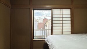 A room with a bed, a window with a view of buildings, and a sliding door. - Spacious 5BR Asakusa Riverside House near Sensoji & Skytree (Taito-Ku)
