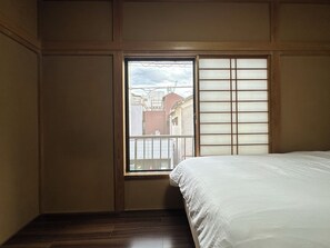 A room with a bed, a window with a view of buildings, and a sliding door. - Spacious 5BR Asakusa Riverside House near Sensoji & Skytree (Taito-Ku)