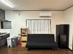 A compact living space with a kitchenette, a bed, a black refrigerator, and a window with sheer curtains. - Vrbo Property (台東区)