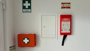 Eine Wand mit Feuerlöscher, Erste-Hilfe-Kasten, Brandmeldebox und Lichtschalter.
