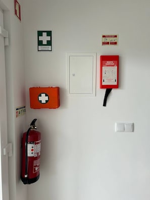 Seinällä on palosammutin, ensiapupakkaus, palohälytyskeskus ja valokytkin.