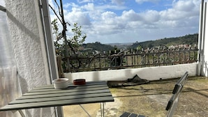 Ein Balkon mit Tisch und Bank, mit Blick auf einen Weinberg und die Ferne.