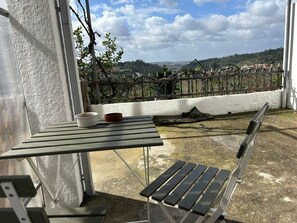 A balcony with a table and bench, overlooking a vineyard and distant landscape. - Apartamento T1 com Terraço (Coimbra)