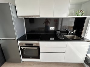 Kompakti keittiö, jossa on jääkaappi, uuni, pesuallas ja musta työtaso.