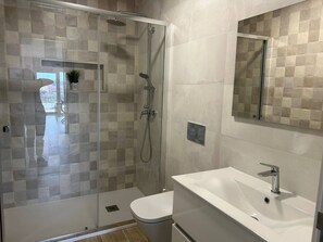 A modern bathroom with a glass-enclosed shower, a white sink, and a mirror. - Apartamento T1 com Terraço (Coimbra)