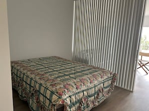 Huone, jossa on sänky, pystylamelliverhoilla varustettu ikkuna ja puulattia.
