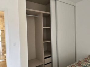 A walk-in closet with multiple shelves and a sliding door. - Apartamento T1 com Terraço (Coimbra)