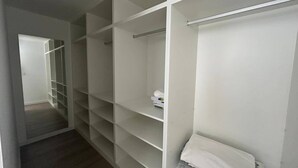 Ein begehbarer Kleiderschrank mit mehreren Regalen und Kleiderstangen, einer sichtbaren Tür und Holzboden.