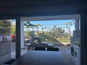A room with a table and chairs, a washing machine, and a view of trees and buildings. - Apartamento T2 com Terraço (Coimbra)