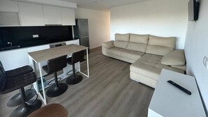 Ein kompakter Wohnbereich mit Küchenzeile, einer Couch, einem Esstisch mit Stühlen und einem Fernseher.