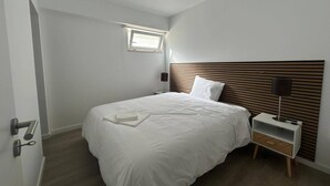 Ein Schlafzimmer mit einem Bett, einem Nachttisch, einer Lampe und einem kleinen Fenster.