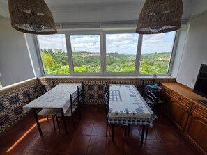 A dining area with two tables, a view of greenery, and a TV on the right. - Quarto Suite Fish QM (Coimbra)