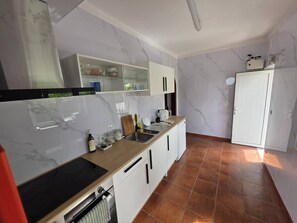 A modern kitchen with white cabinets, a black stove, and a tiled floor. - Quarto Suite Fish QM (Coimbra)