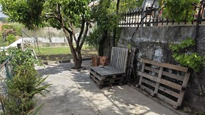 A concrete patio with a wooden bench, a stack of firewood, and a metal fence. - Quarto Suite Hope Vista Jardim (Coimbra)