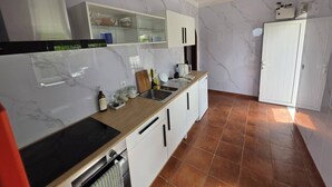 A modern kitchen with white cabinets, a black stove, and a tiled floor. - Quarto Suite Hope Vista Jardim (Coimbra)