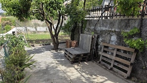 Un patio de concreto con un banco de madera, leña apilada y una cerca metálica.
