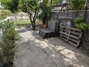 A concrete patio with a wooden bench, a stack of firewood, and a metal fence.