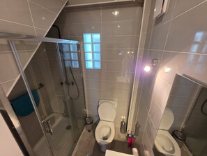A modern bathroom with a glass-enclosed shower, two toilets, and a small window. - Quarto Sunrise com Varanda e WC (Coimbra)