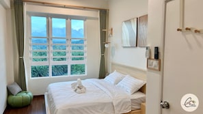 A bedroom with a large window, a bed, a bedside table, a lamp, and a door. - Trival Blessing Cottage Homestay @ Sri Indah Sandakan (Sandakan)