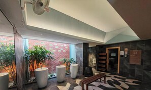 A modern lobby with a fan, large planters, a sauna sign, and a bench.